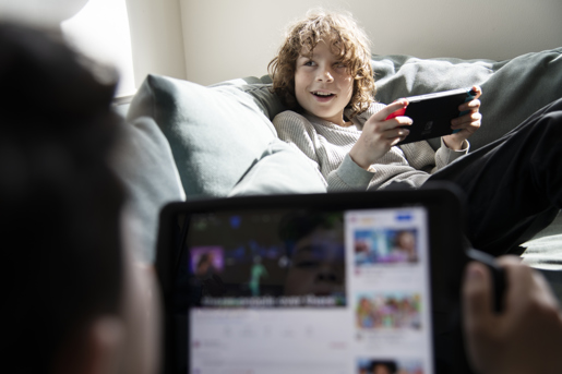 To børn sidder i en sofa med en iPad og en Gameboy